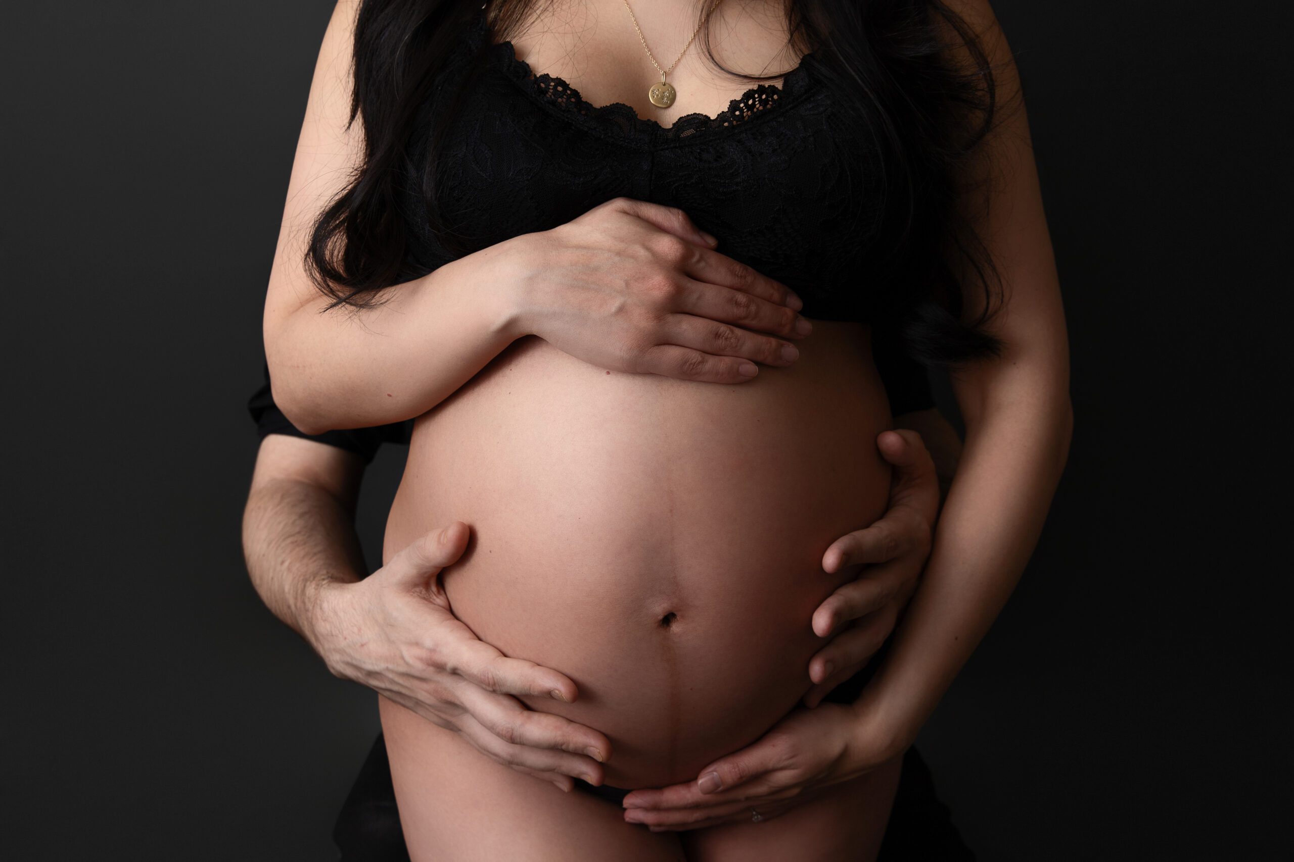 Pregnant belly with hands in a soft studio maternity session by a West Island maternity photographer